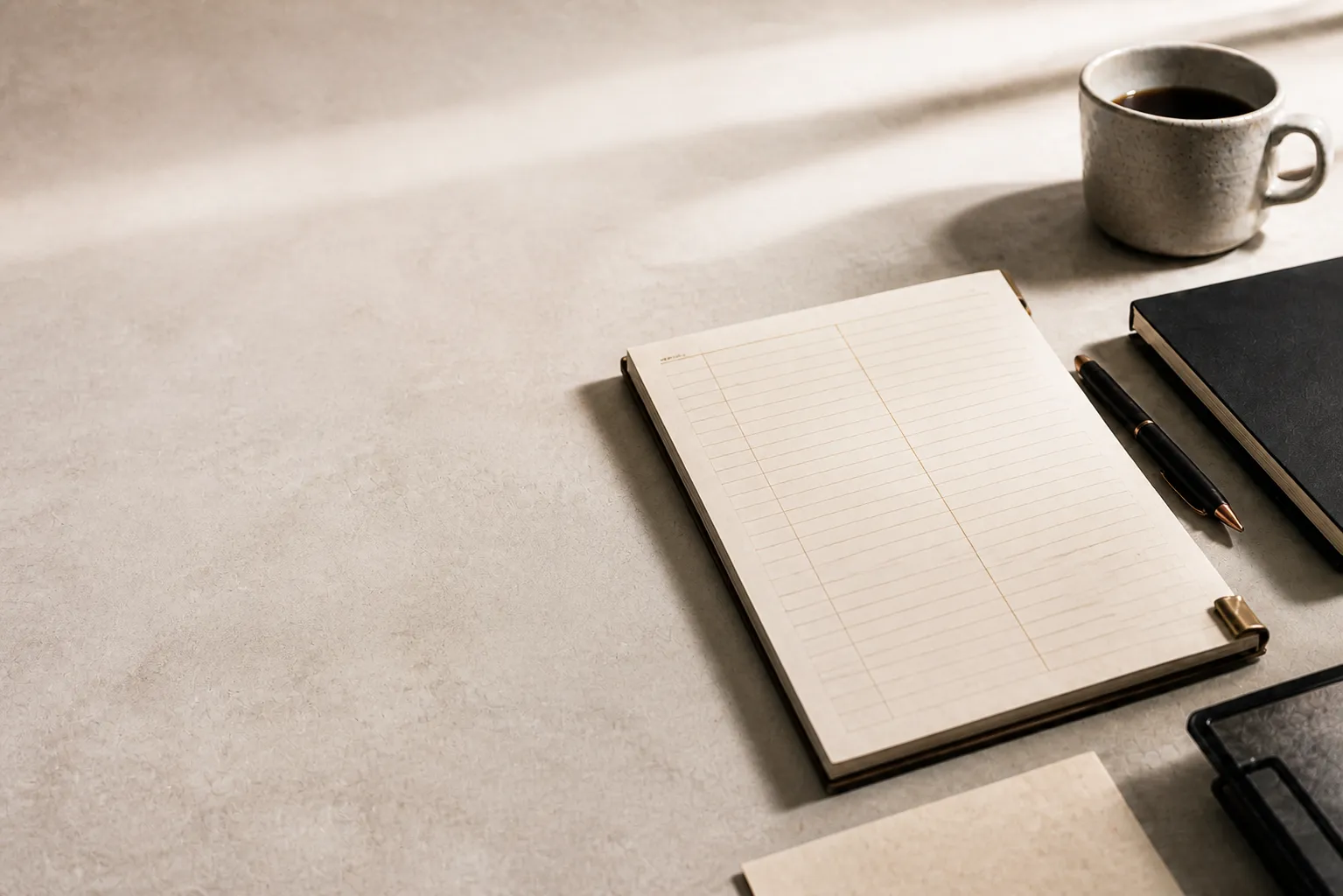 A warm work desk with a ledger, notebook, pen and coffee